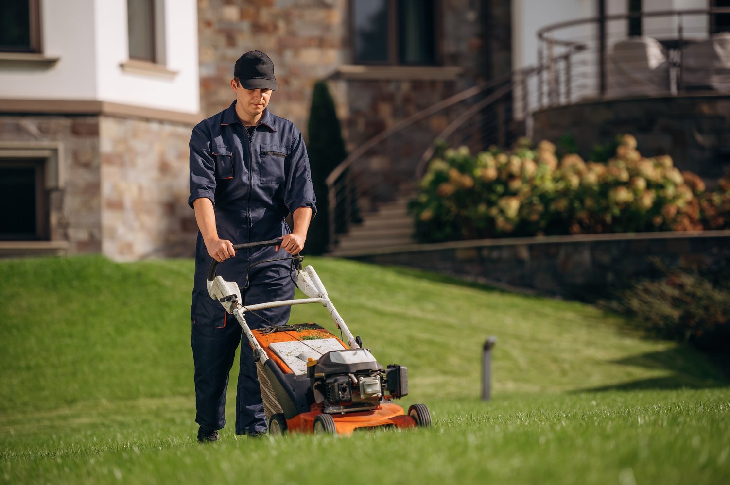 Fuel powered lawn mover, cutting the grass. Professional gardener is on the lawn.
