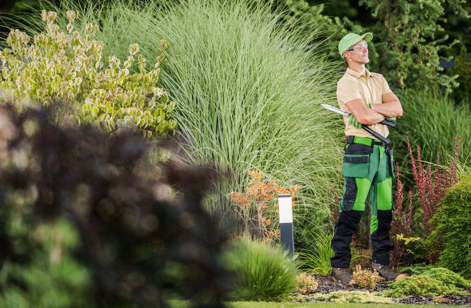 Professional Garden Worker with Pro Scissors in His Hands Staying Next to Beautiful Backyard Garden